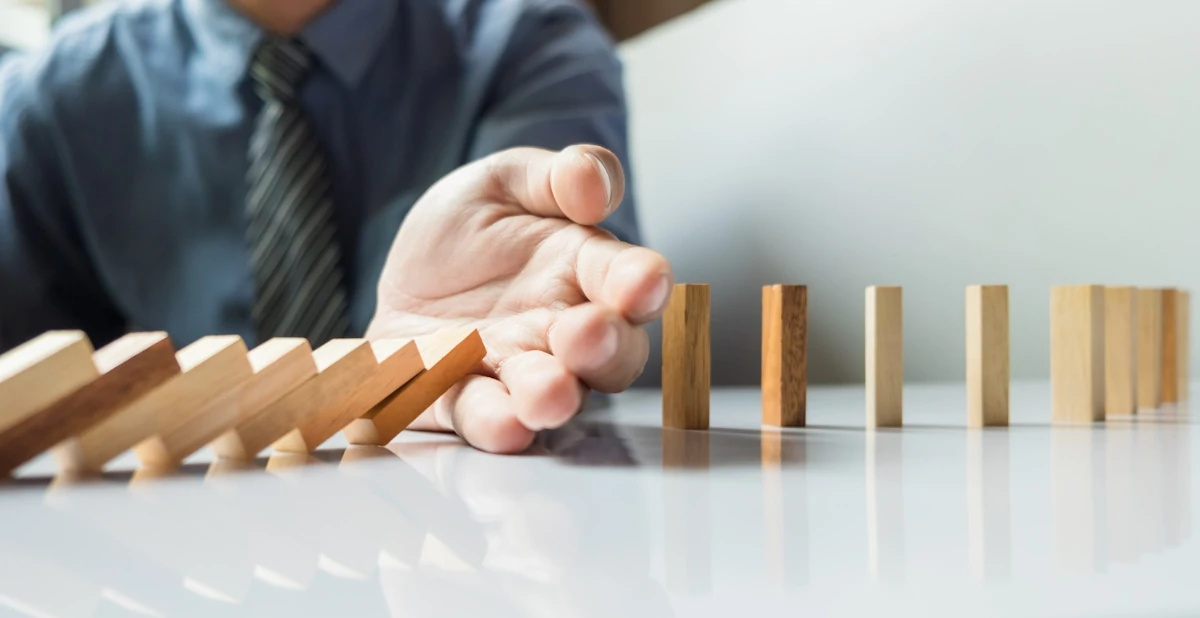 image representing a businessman hand stop dominoes from falling apart